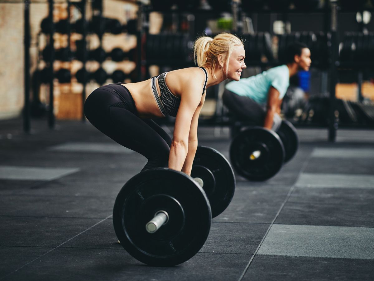 2 Day Gym Workout Plans to Get Strong and Athletic w/ PDF A female is lifting a barbell